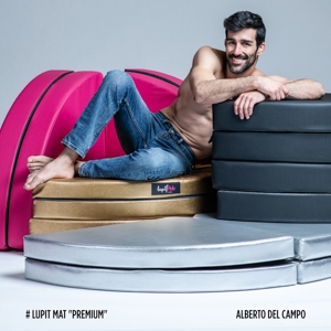 Lupit Pole various Crash Mats Pole Dancing Mats stacked, with Alberto del Campo sitting on them, wearing only jeans.